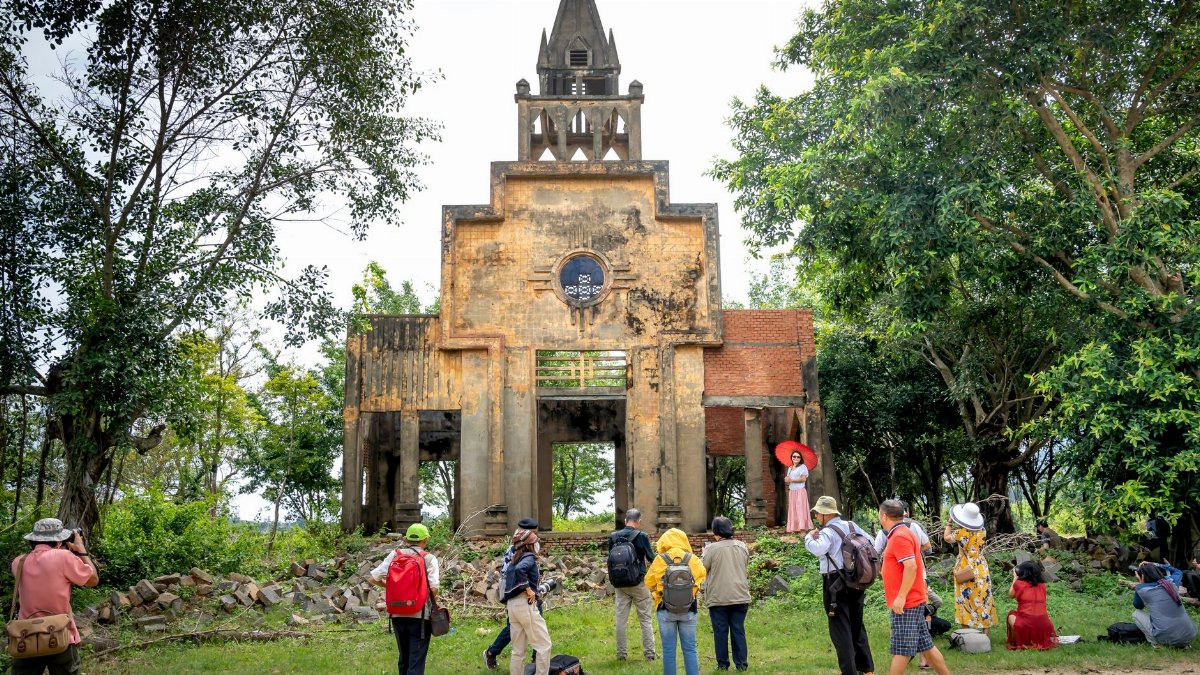A group of tourists visits a historic, abandoned church ruin surrounded by lush greenery.
