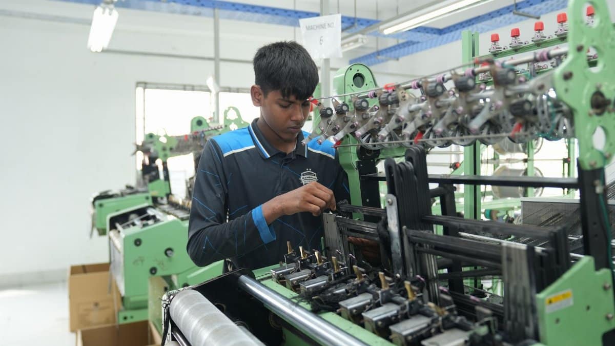 A young man focuses on operating a textile machine in a modern factory setting.