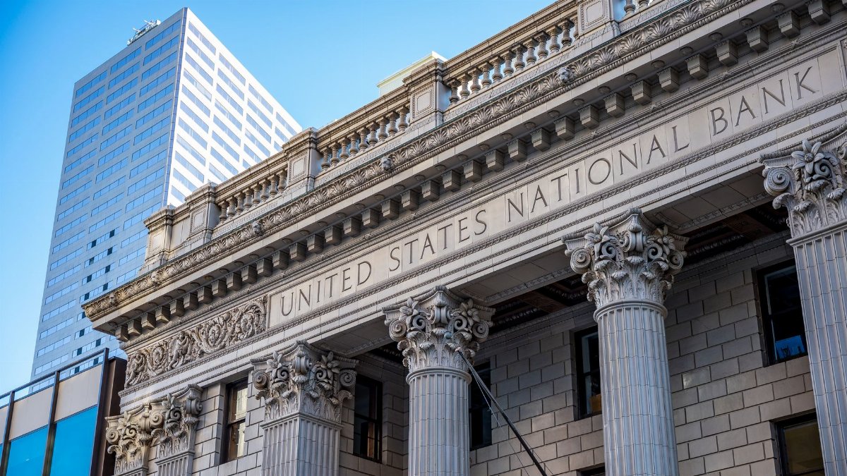 Exterior of historic national bank with decorative elements on classic columns located in city with modern building against blue sky