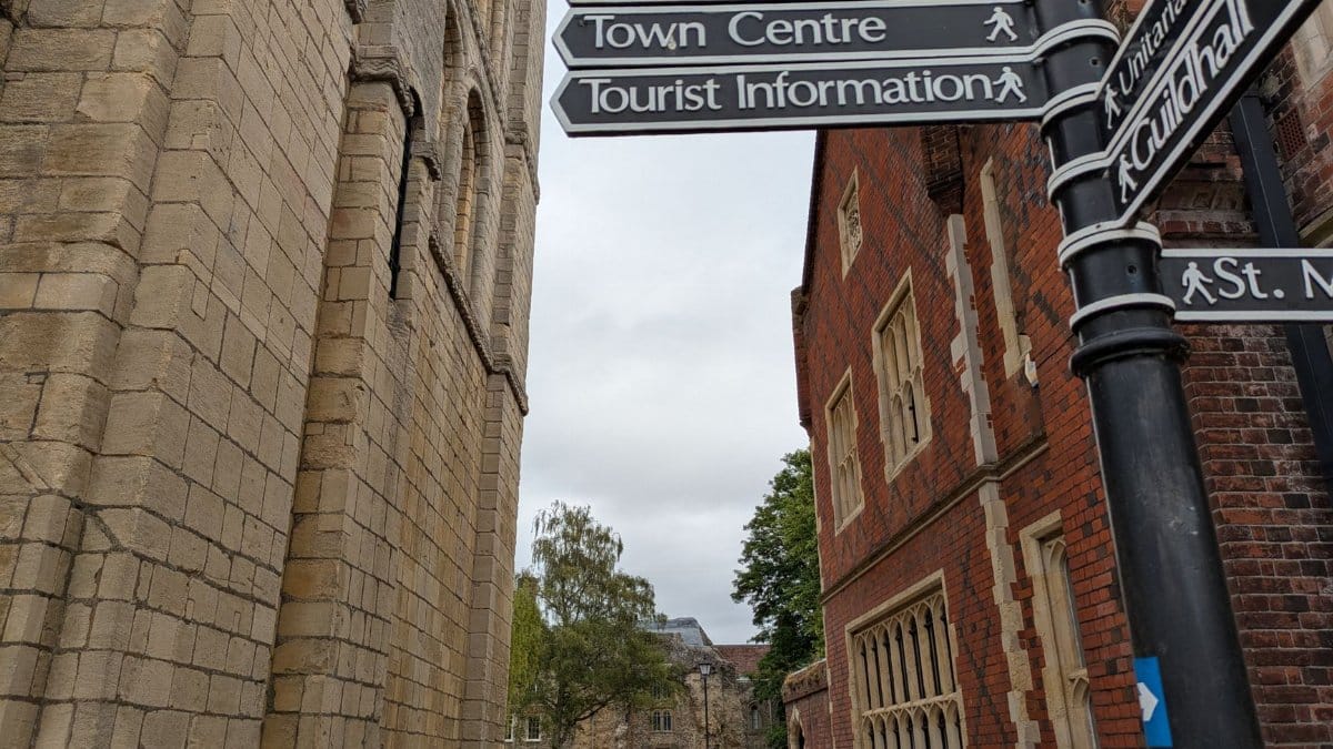 Directional signpost in a historical town center near Abbey Gardens.