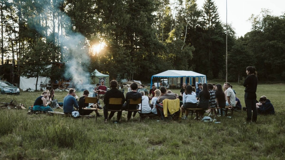 A group of adults relaxing around a campfire in a scenic outdoor setting with tents.
