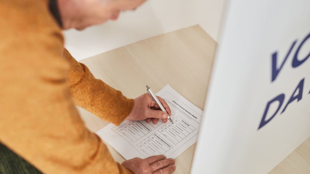Senior man marking a ballot at a voting booth in an indoor polling station.