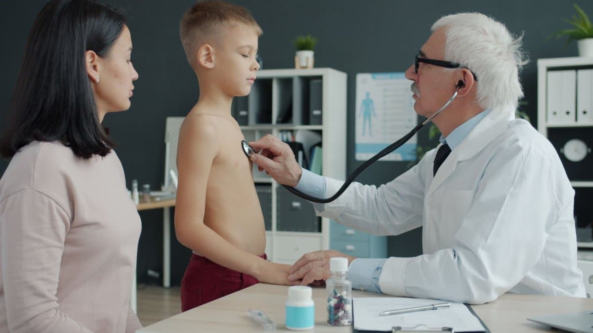 A doctor uses a stethoscope to examine a young boy with his mother present in a medical office.