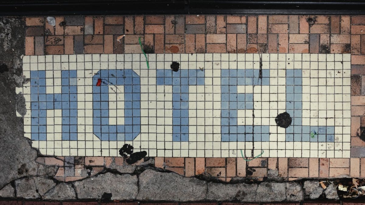 A close-up view of a vintage hotel sign in blue on a mosaic floor, with signs of weathering and age.