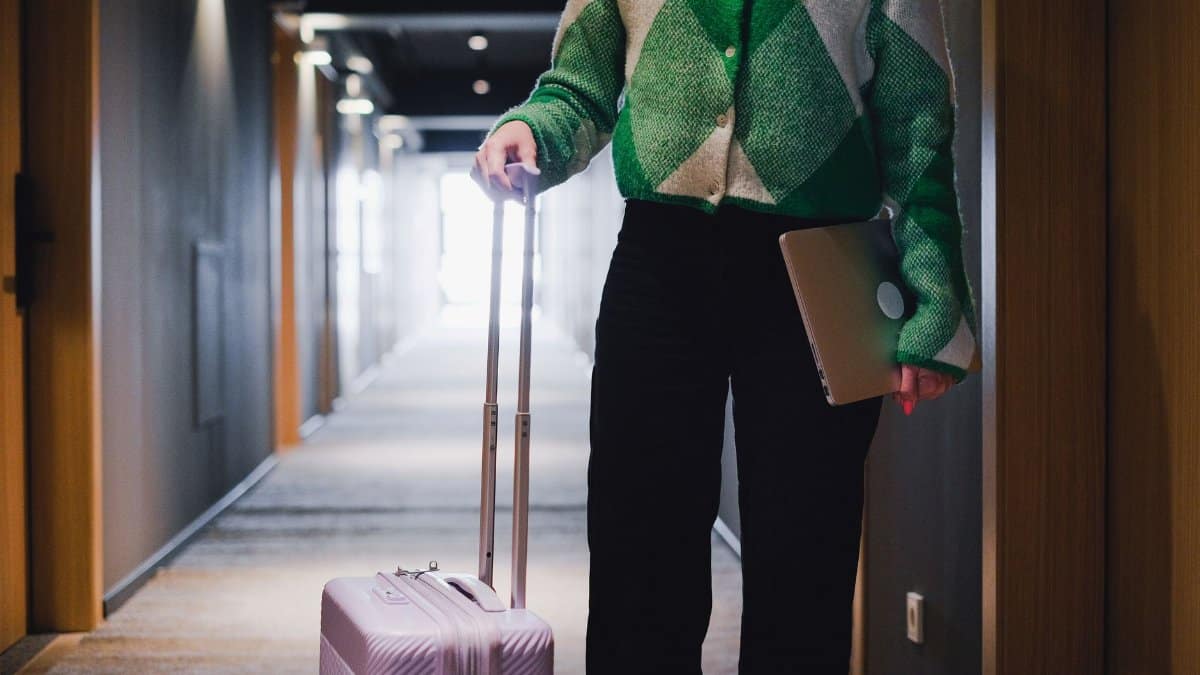 A person in a hotel corridor holding luggage and a laptop, showcasing travel and business.
