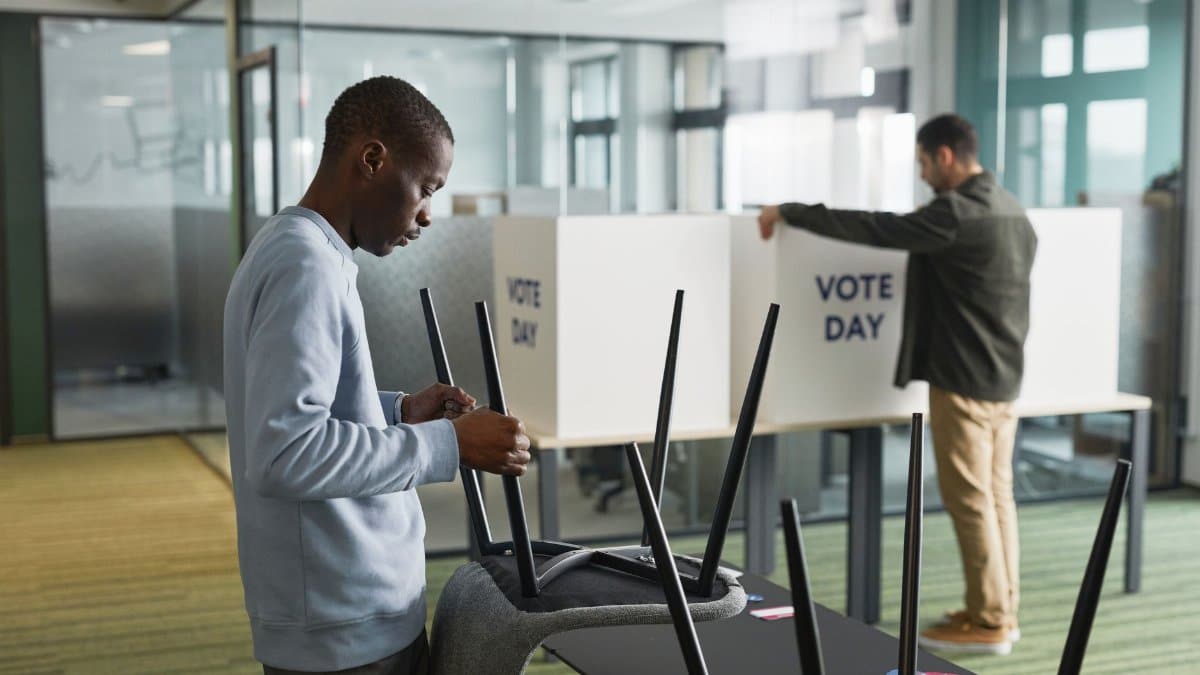 Men preparing voting booths indoors for election day, enhancing democracy.