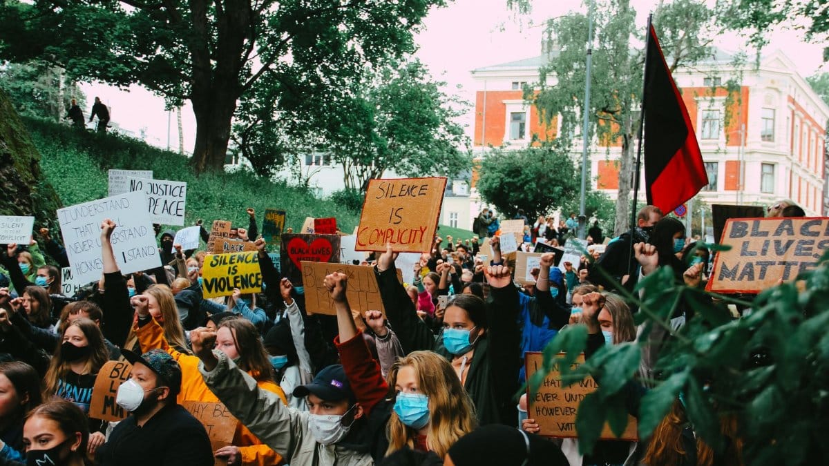 A crowd of diverse protesters holding signs and wearing masks in a peaceful Black Lives Matter rally.