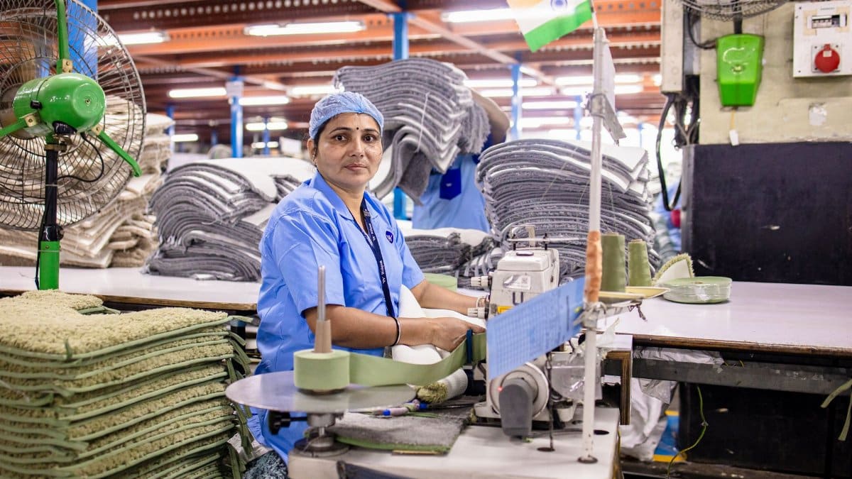 A female factory worker sewing textiles in an Indian factory, surrounded by fabrics.