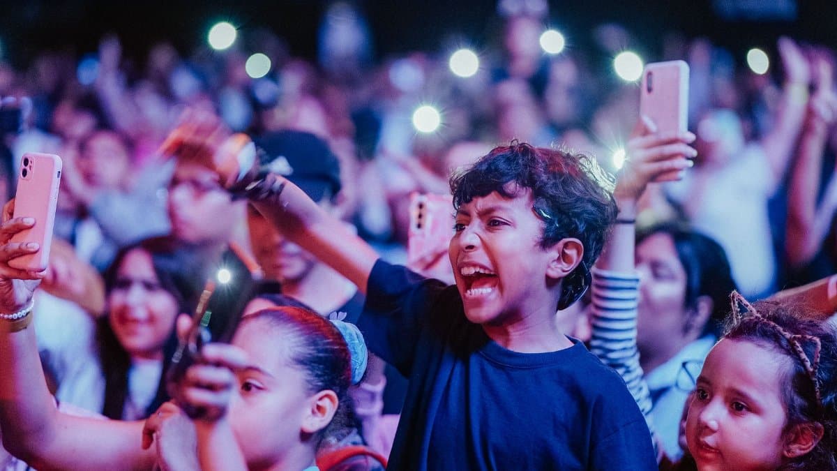 Energetic kids enjoy a vibrant music concert, capturing moments on smartphones.