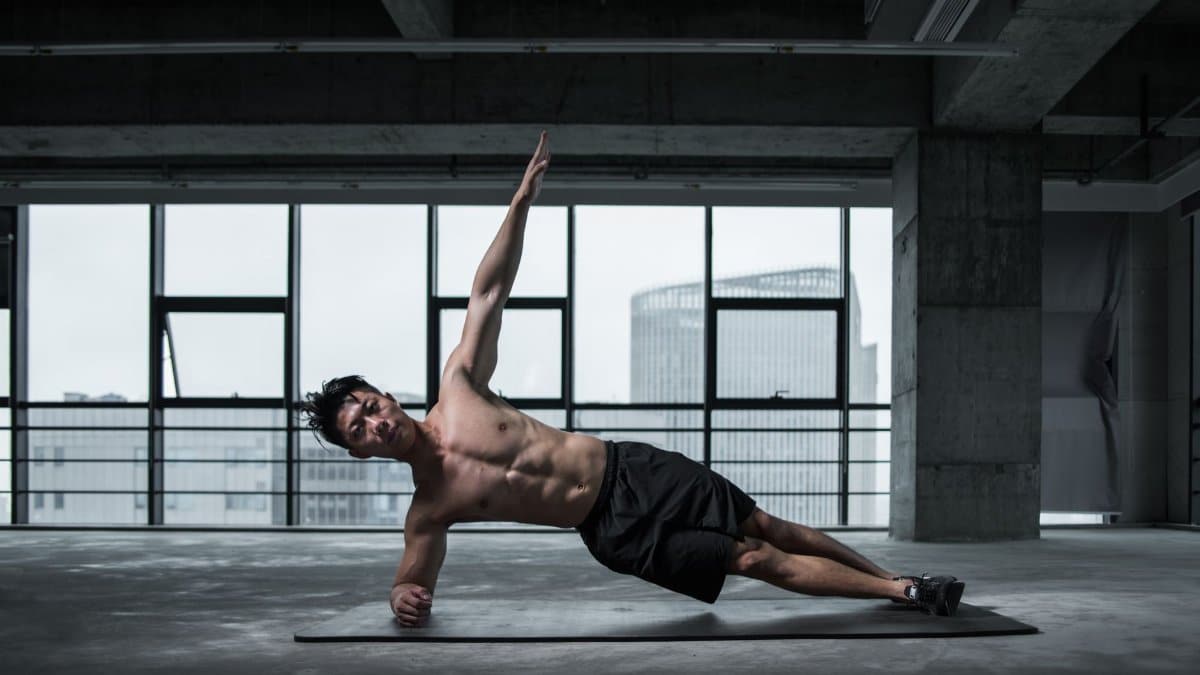 Fit man doing a side plank in an urban indoor gym, showcasing core strength and balance.