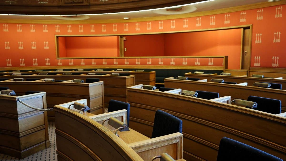 An empty parliamentary meeting room with wooden seating and vibrant orange walls in Oslo, Norway.