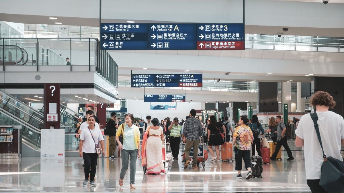 Crowded Hong Kong airport terminal with diverse passengers and informative signage.