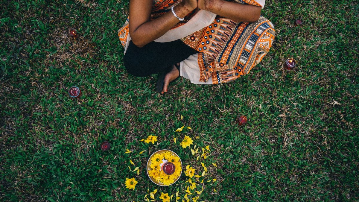 Top view of an Indian woman in traditional clothing arranging flowers on grass, reflecting cultural traditions.