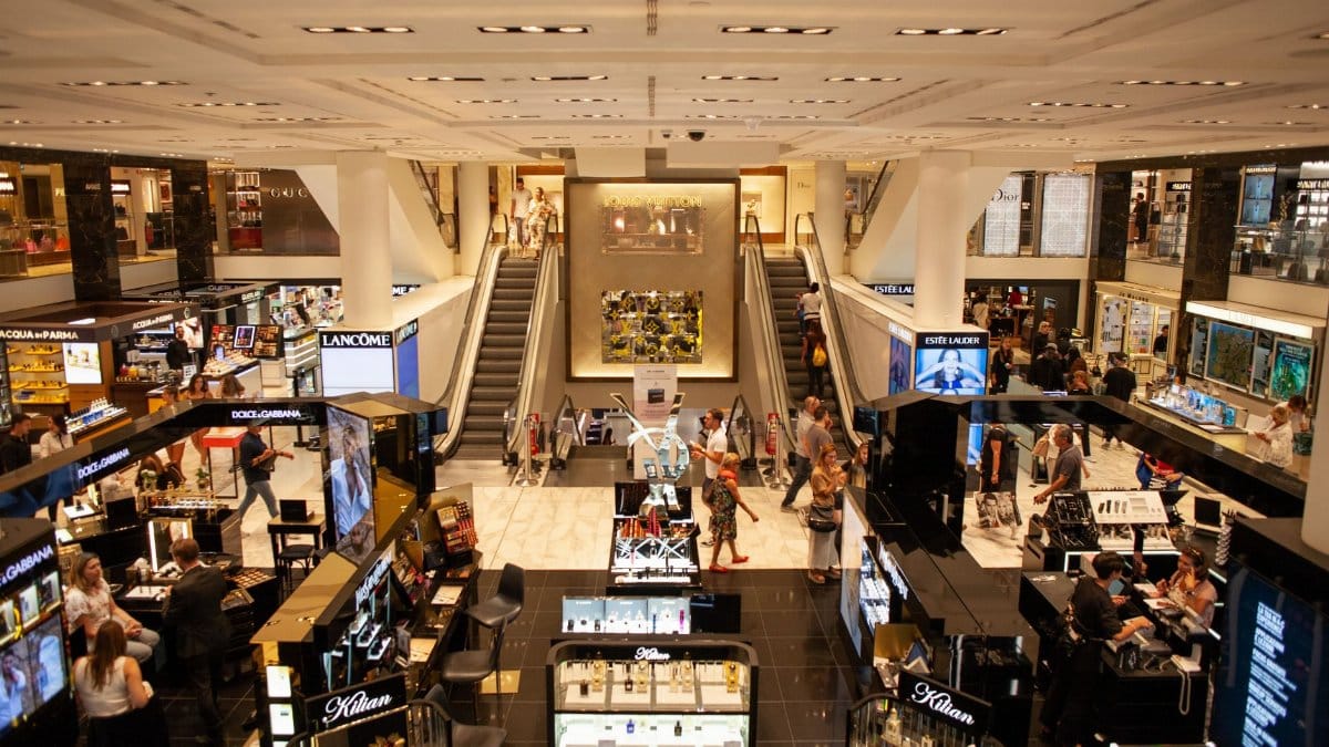 A bustling scene inside a modern shopping mall with escalators and various retail stalls.