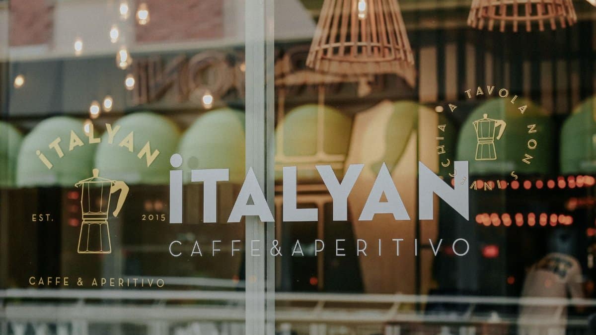 Close-up of glass window with Italian cafe branding and reflections.