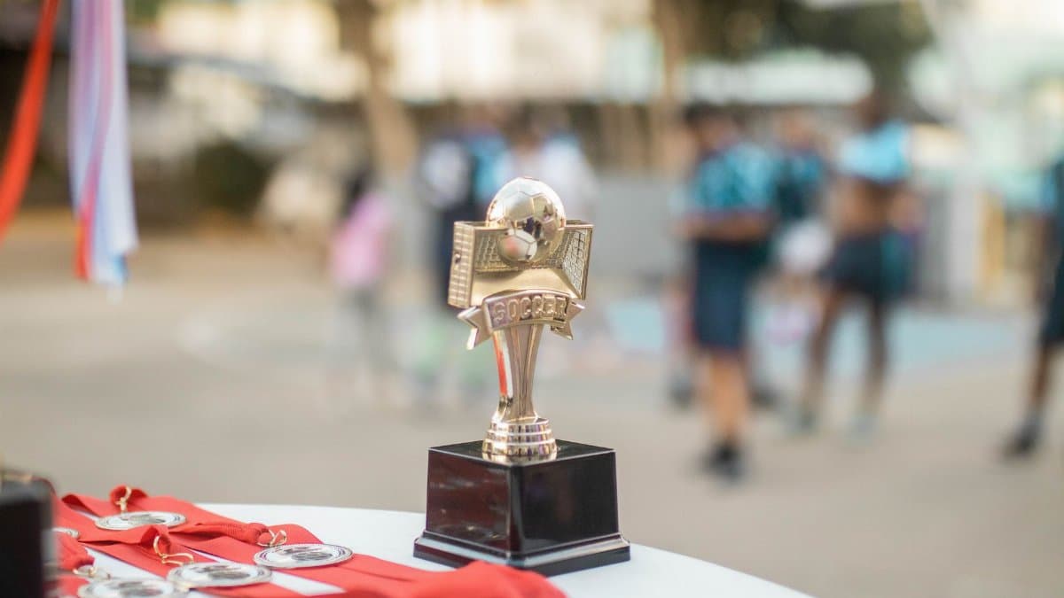Close-up of a polished soccer trophy with medals at an outdoor sports award ceremony.