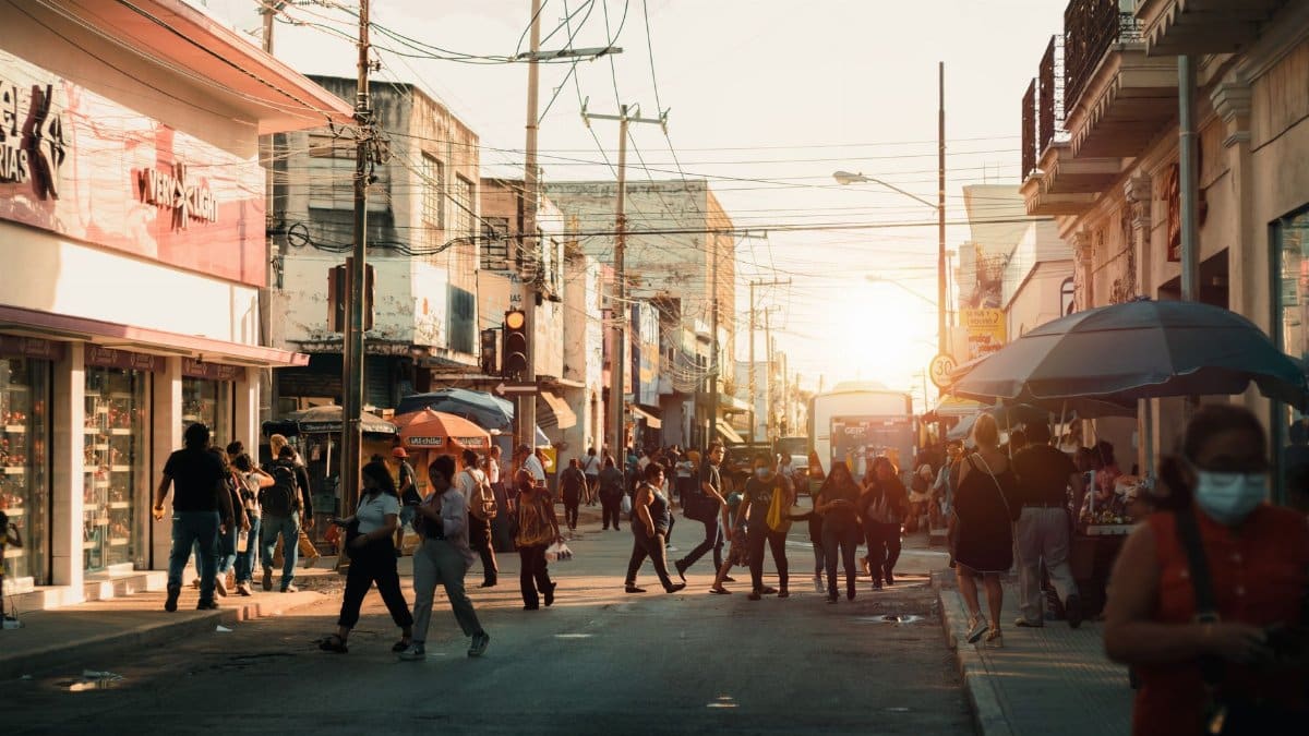 A lively city street filled with people walking and shopping during sunset, capturing urban life.