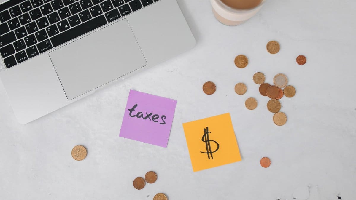 A workspace with a laptop, sticky notes, coins, and a coffee cup, ideal for tax planning.