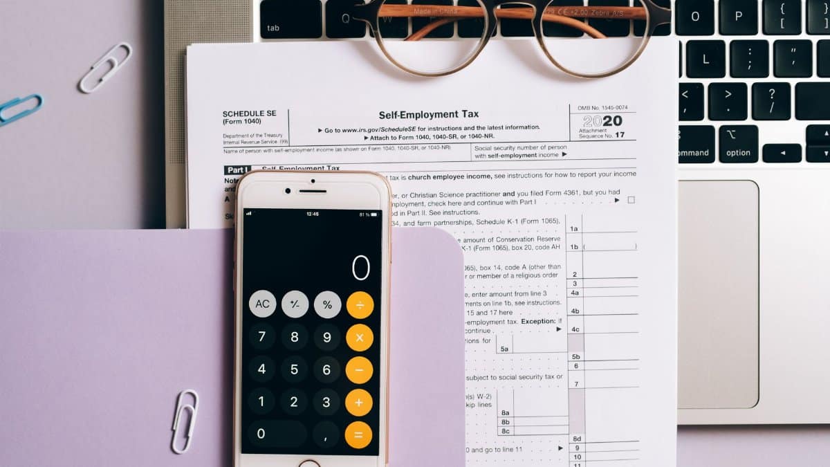 Flat lay of tax documents, smartphone calculator, and laptop for self-employment accounting.