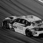 A dynamic black and white photo of a high-speed race car on a track, capturing motion and speed.