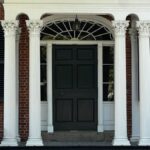 Colonial style house entrance with white columns and black shutters. Traditional architectural design.