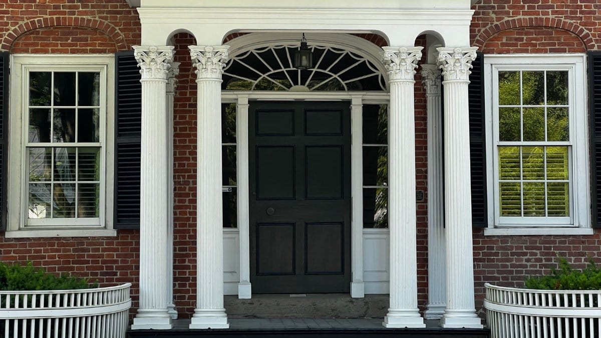 Colonial style house entrance with white columns and black shutters. Traditional architectural design.