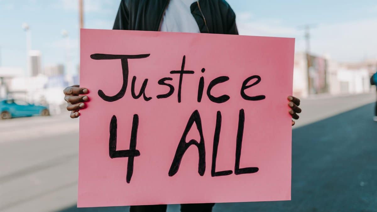 A protester holds a pink 'Justice 4 All' placard on an urban street.