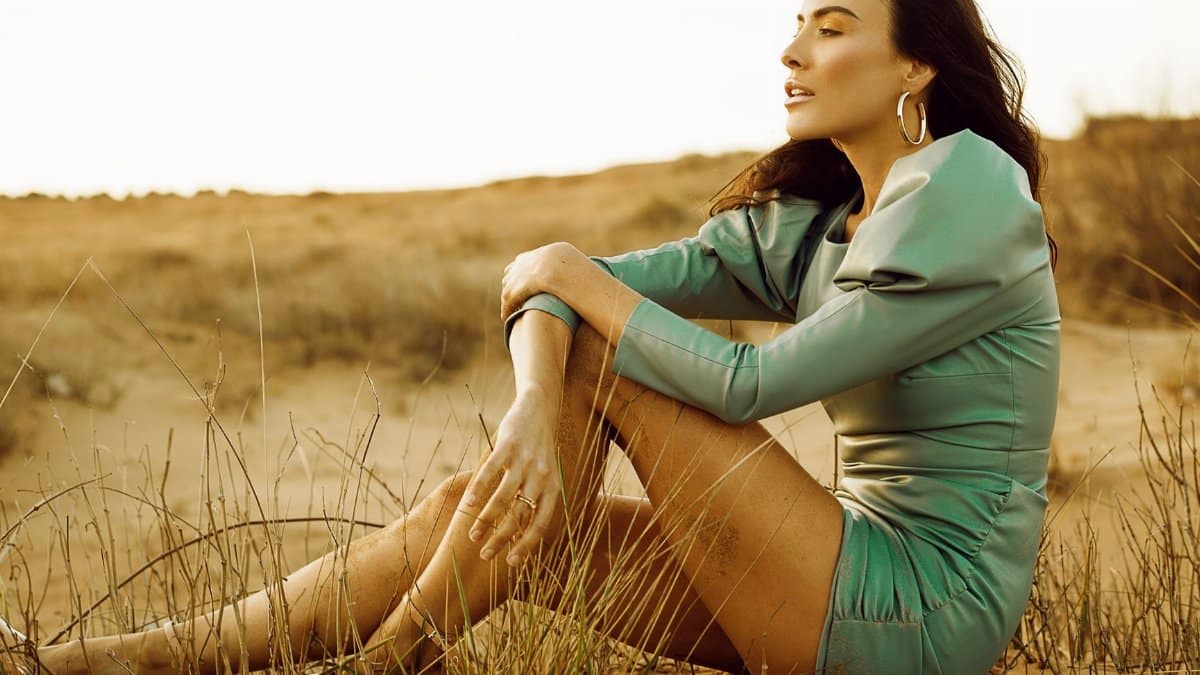 A stylish woman in a blue dress sits on sand dunes, capturing the essence of outdoor fashion and tranquility.
