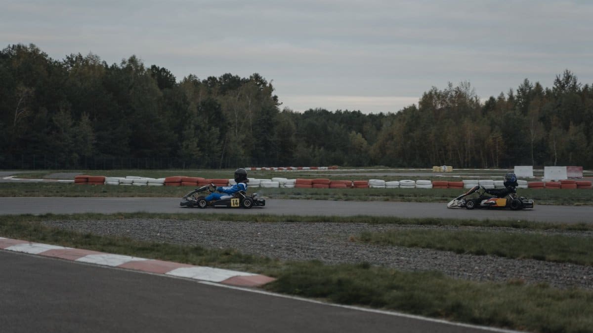Two go-karts racing on an outdoor track surrounded by trees under a cloudy sky.