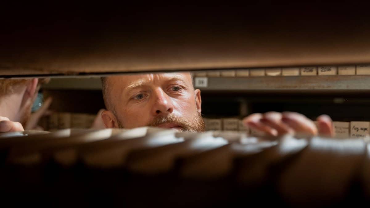A man searches through archives in an office storage room, focused and working.