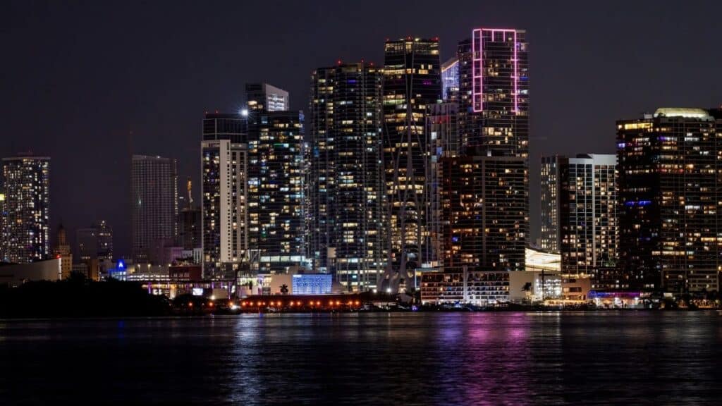 A stunning view of Miami's illuminated skyline reflecting on water at night.