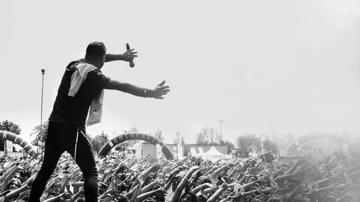 Dynamic black and white image of a live concert with an engaging performer facing a lively crowd outdoors.