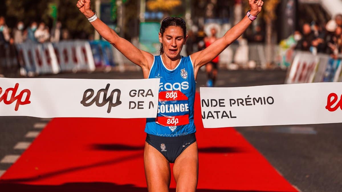 Triumphant sportswoman crosses marathon finish line with arms raised in victory outdoors.