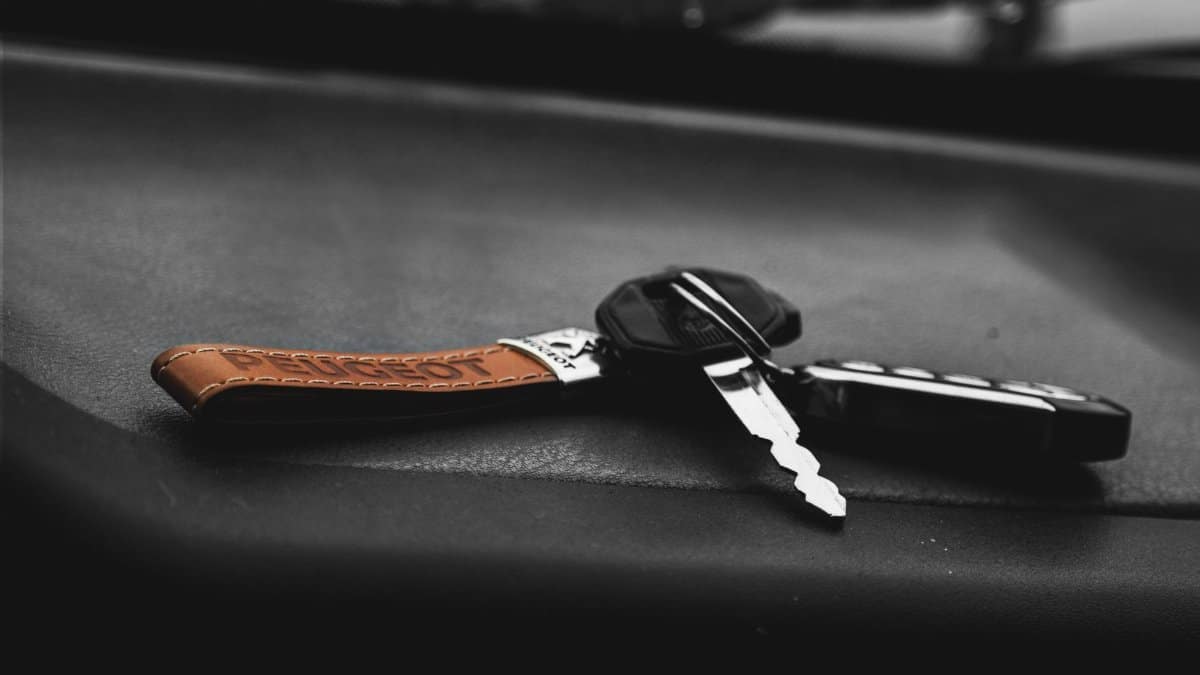 High contrast, artistic shot of a car key on a black surface with a leather keychain.