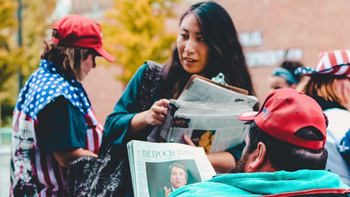 A group of adults reading newspapers outdoors, immersed in political discussions on a vibrant day.
