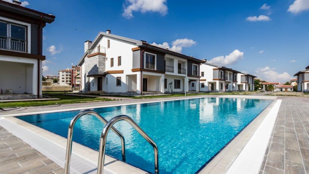 Luxury modern villas surrounding a glistening swimming pool under a clear blue sky.