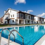 Luxury modern villas surrounding a glistening swimming pool under a clear blue sky.