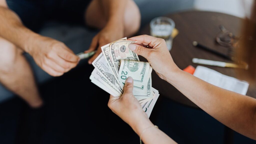 Close-up of people handling and counting US dollar bills indoors.