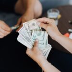 Close-up of people handling and counting US dollar bills indoors.