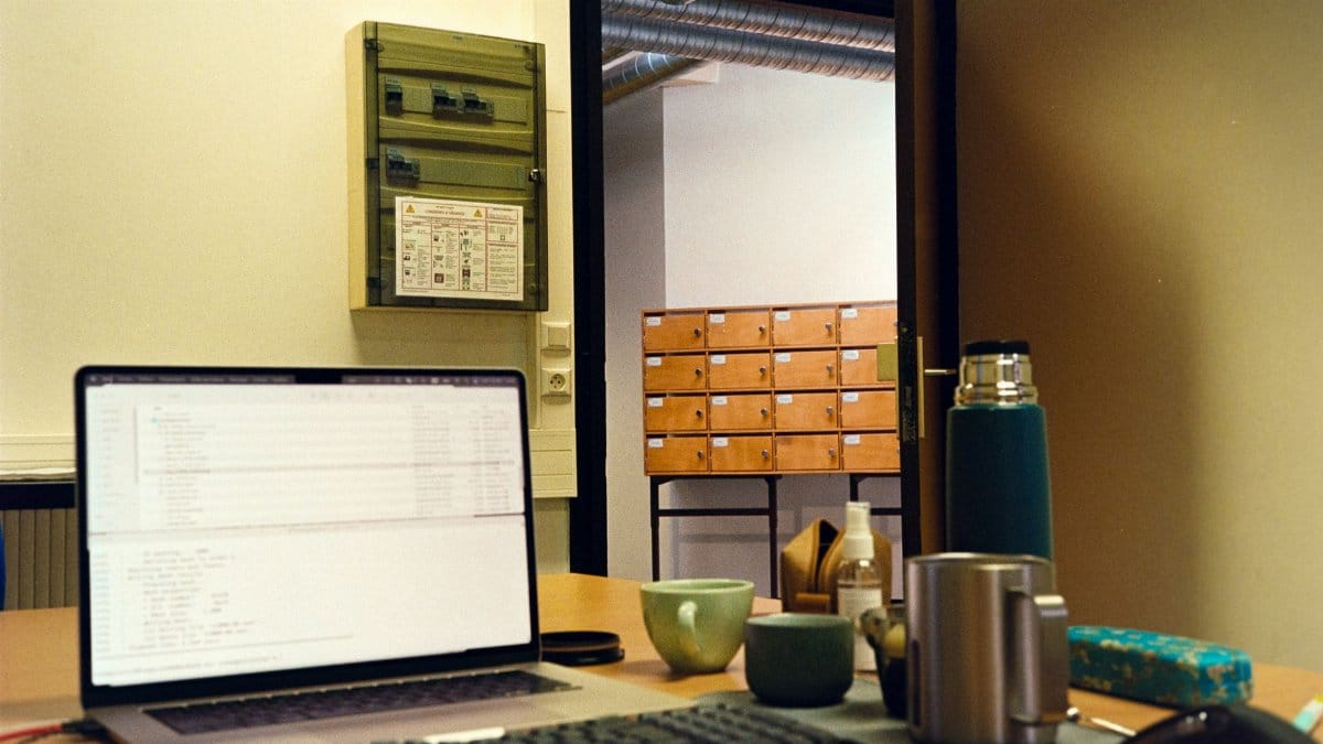 A cozy office workspace featuring a laptop, mugs, and storage drawers in a warm setting.