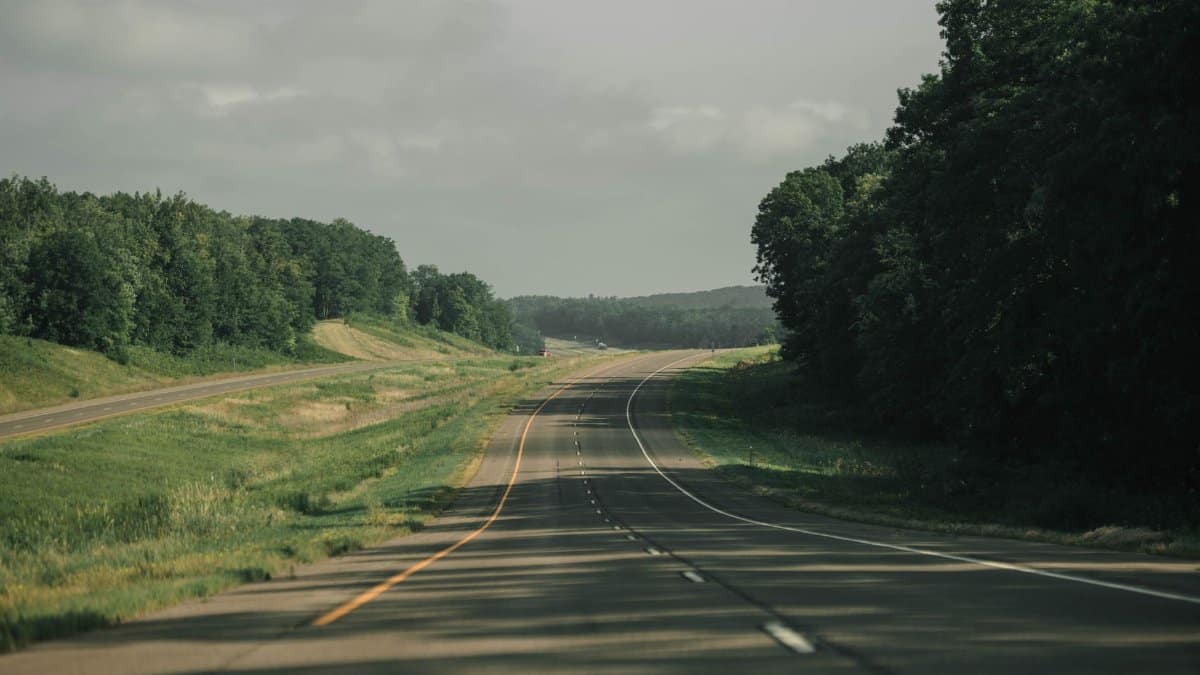 A peaceful highway running through lush greenery in Minnesota under a cloudy sky.