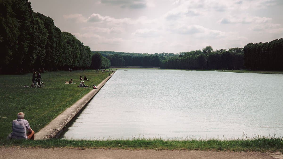 People enjoying a sunny day by the canal in the gardens of Versailles.