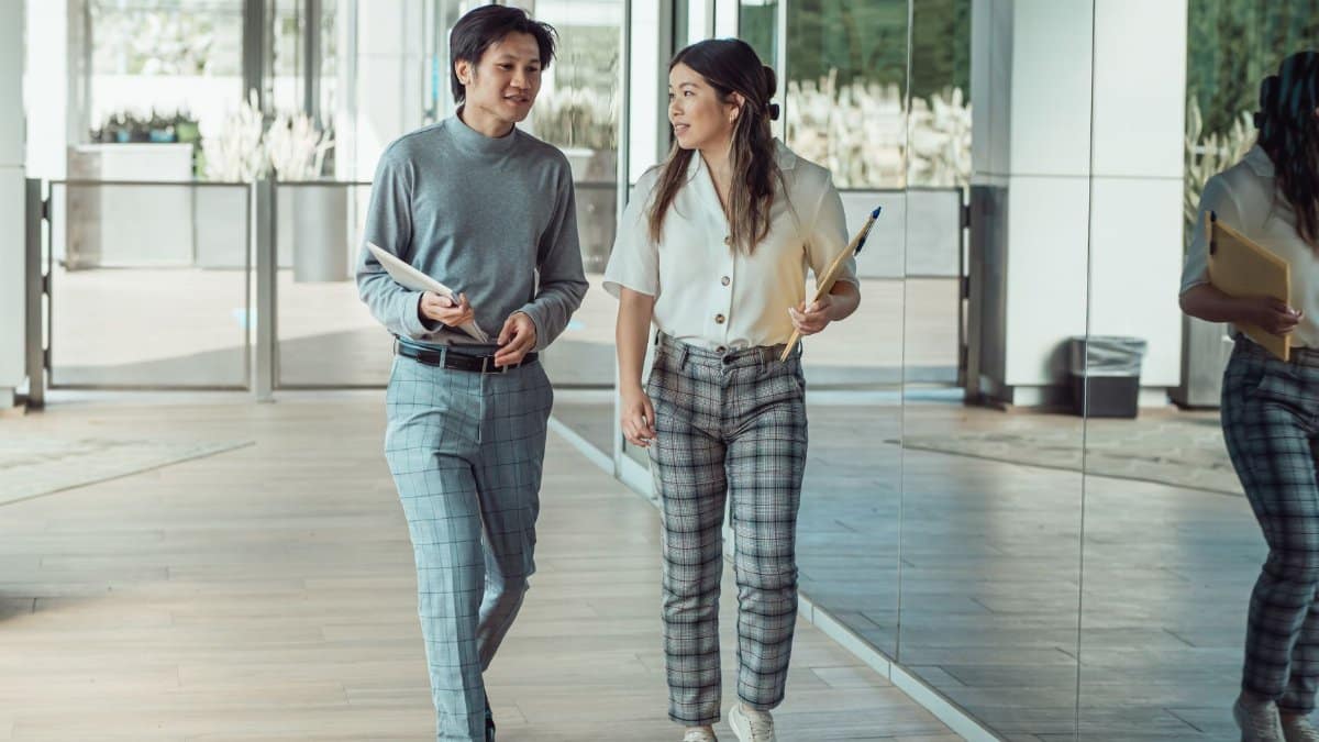 Two colleagues engaged in conversation while walking through a modern office hallway.