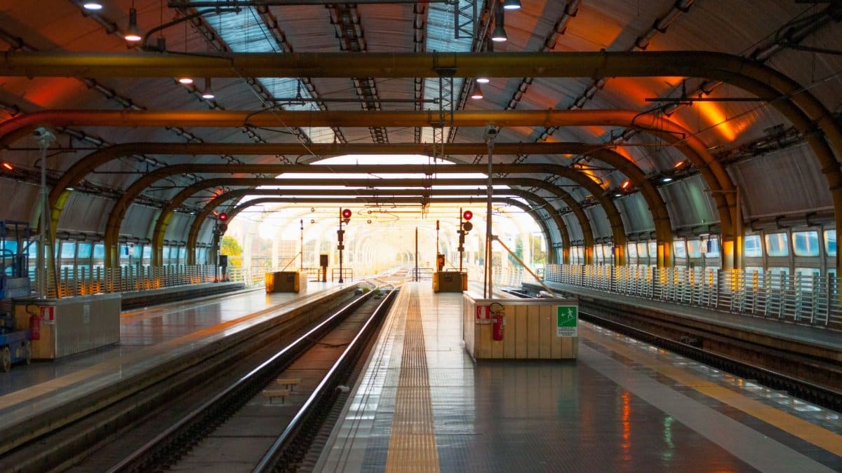 Contemporary railway station featuring a well-lit empty platform and tracks under a steel arch structure.