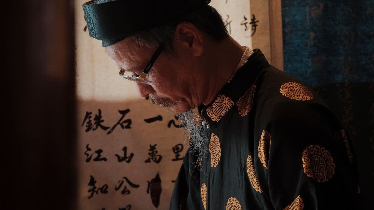 Elderly Vietnamese man practicing calligraphy in traditional attire. Serene and cultural moment captured.