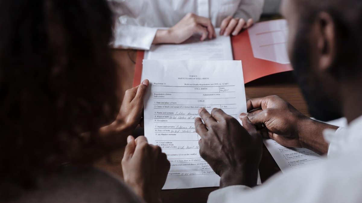 A couple collaboratively signs legal documents in the presence of an advisor.