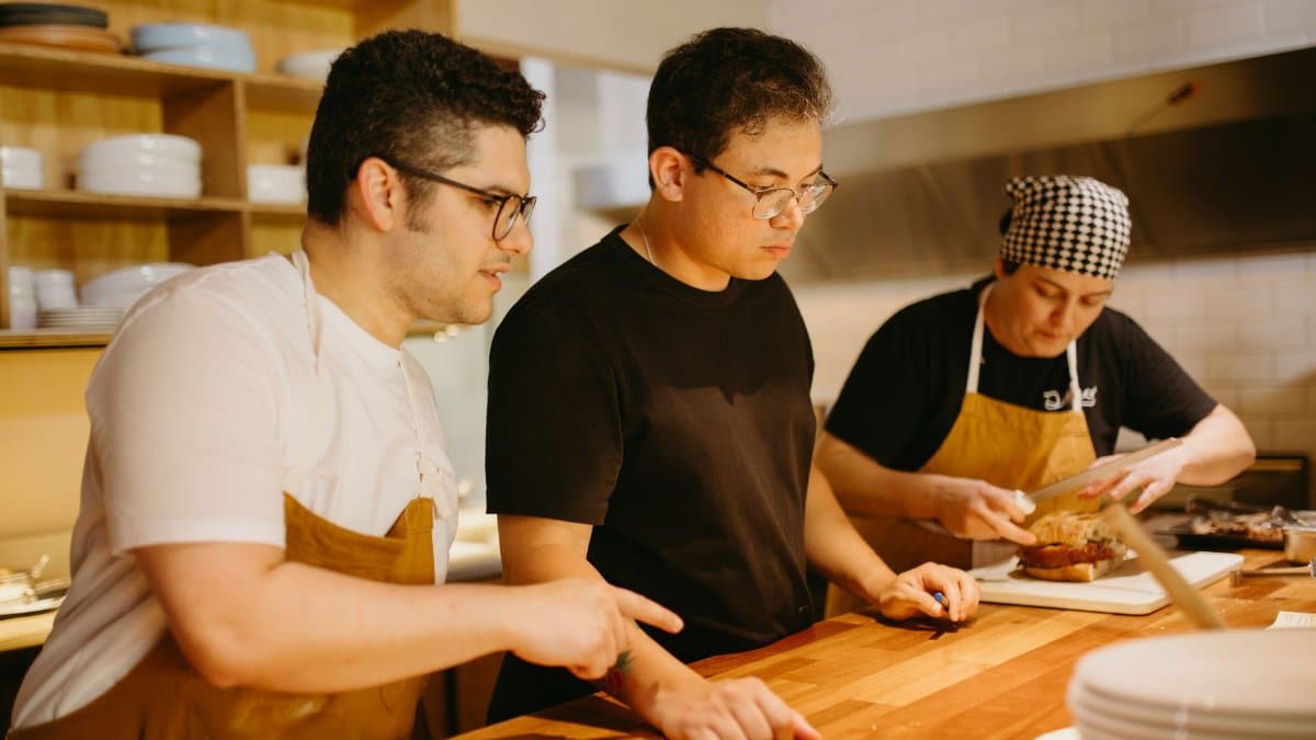 Three chefs working together at a kitchen counter, preparing dishes with focus and teamwork.