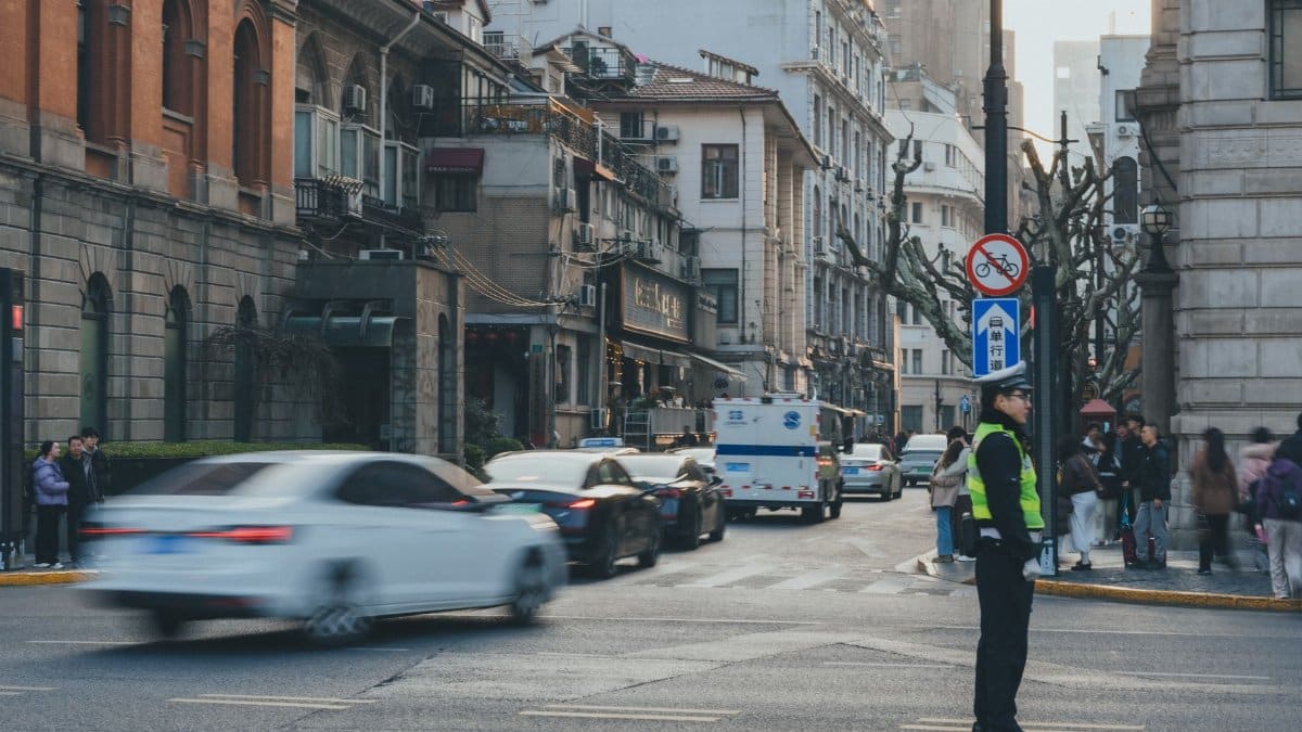 An urban street bustling with cars and people, featuring a traffic officer directing vehicles in a vibrant cityscape.
