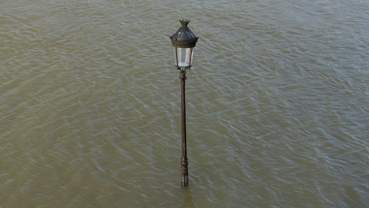 A lone streetlamp is submerged in flood waters, highlighting the impact of urban flooding.