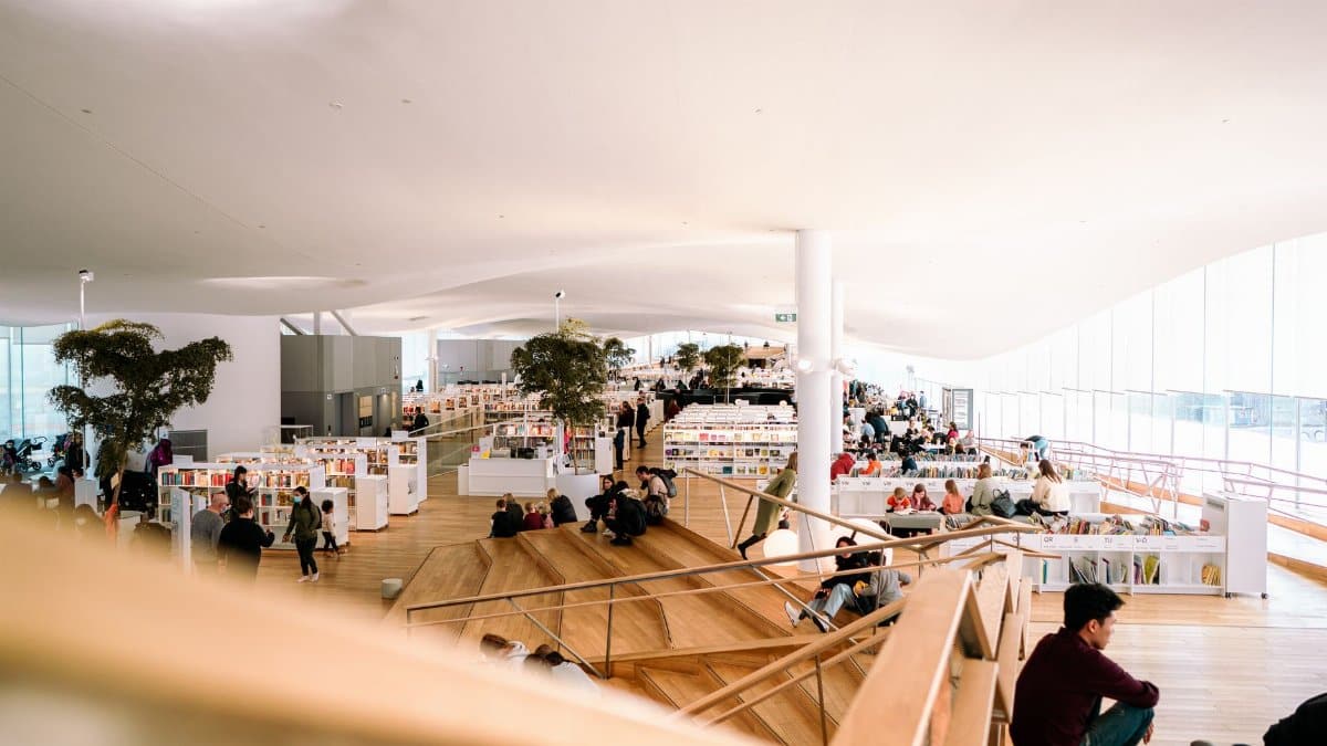 Contemporary library interior filled with people reading and relaxing in a bright and open space.